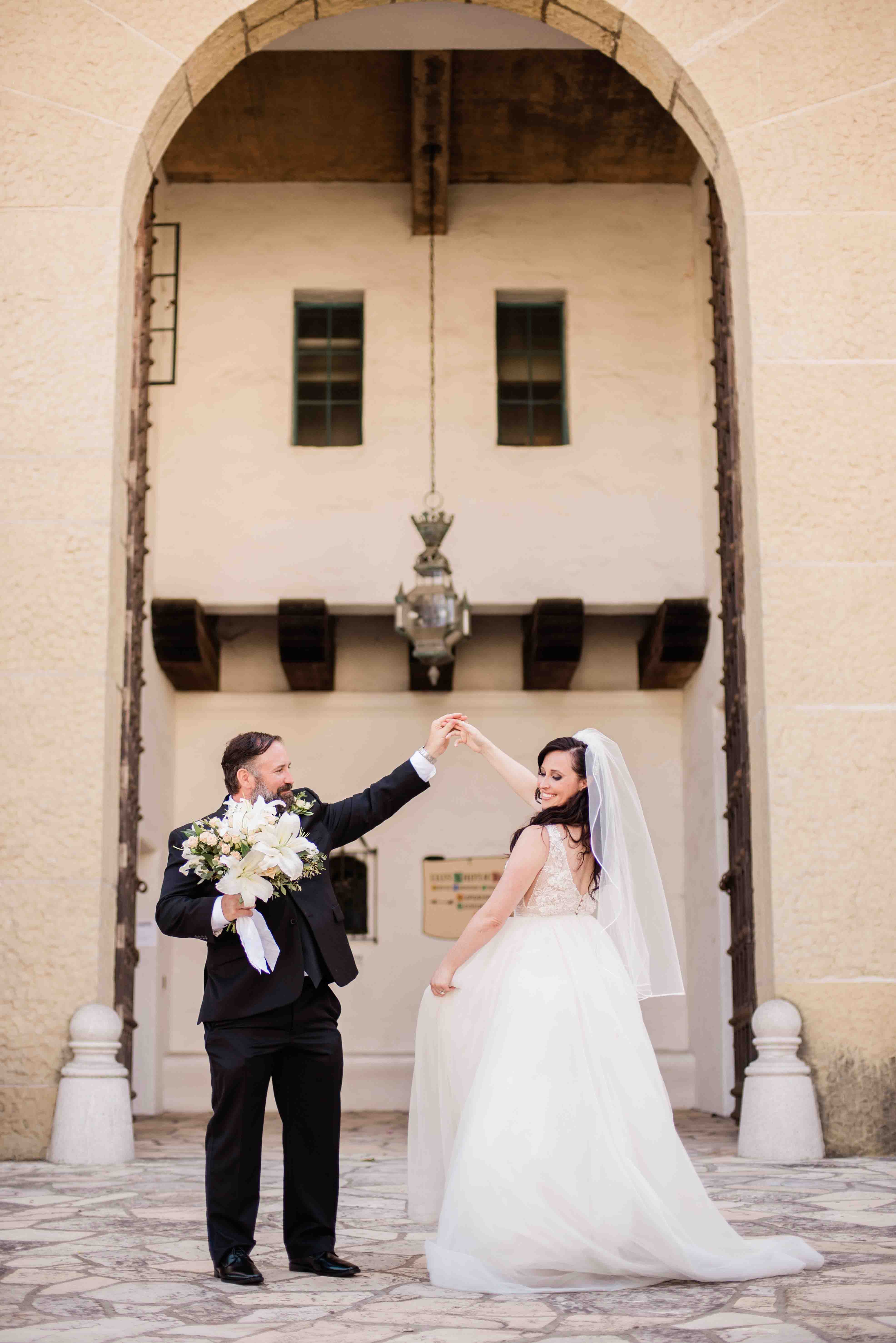groom twirling bride around in front of large archway